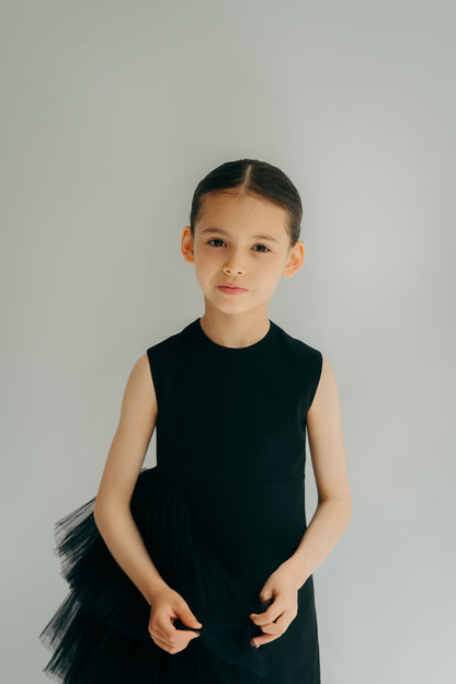 Young girl wearing a black straight dress with asymmerical tulle detail