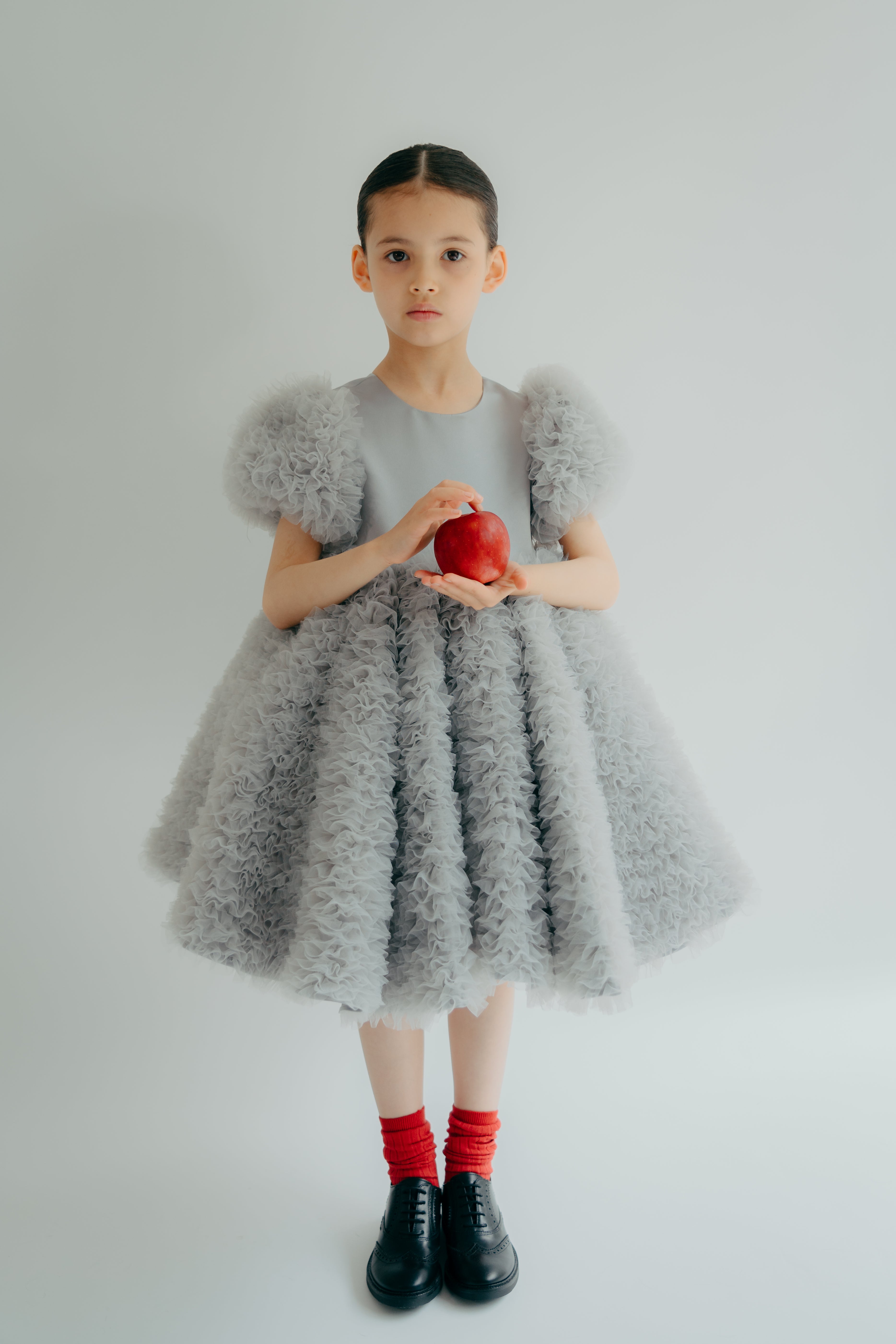 Young girl wearing a frilly grey dress holding a red apple
